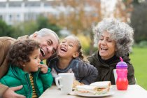 Verspielte Großeltern und Enkel lachen, essen Mittagessen im Park — Stockfoto