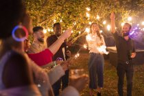 Playful friends with sparklers enjoying garden party — Stock Photo