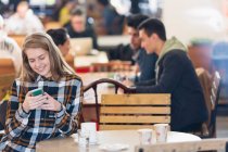 Усміхнена молода жінка використовує смартфон у кафе — стокове фото