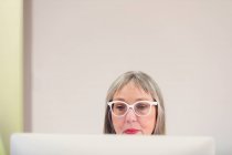 Mujer madura enfocada en anteojos usando computadora - foto de stock