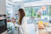 Woman with digital tablet at refrigerator in kitchen — Stock Photo
