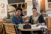 Portrait confident young male college students studying at cafe table — Stock Photo