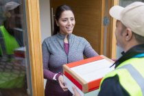 Sorrindo mulher receber pacote de entregador na porta da frente — Fotografia de Stock
