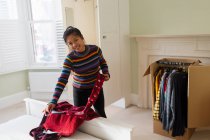 Retrato mulher desempacotando roupas de caixa móvel no quarto — Fotografia de Stock