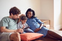 Junge schwangere Familie nutzt Smartphone auf Wohnzimmersofa — Stockfoto