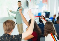 High school students with hands raised during lesson in classroom — Stock Photo