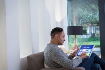 Человек, устанавливающий умную домашнюю сигнализацию с цифрового планшета на диване гостиной — стоковое фото