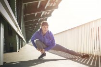Joven corredora femenina enfocada estirando piernas en la soleada plataforma de la estación de tren - foto de stock