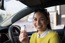 Portrait happy young woman holding new drivers license in car — Stock Photo