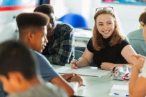 Lächelnde Gymnasiastin im Gespräch mit Mitschülern im Klassenzimmer — Stockfoto