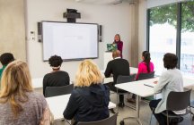Female community college instructor leading lesson at projection screen in classroom — Stock Photo