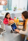 Filha assistindo mãe usando tablet digital na cozinha — Fotografia de Stock