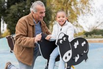 Портрет улыбающегося дедушки и внучки, играющих на детской площадке — стоковое фото