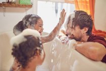 Le figlie giocose in bagno di bolla che asciugano bolle su faccia di padri — Foto stock