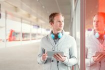 Молодий чоловік з цифровим планшетом і навушниками чекає біля платформи вокзалу — стокове фото