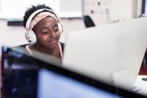 Sonriente estudiante universitaria comunitaria con auriculares en la computadora en el aula - foto de stock