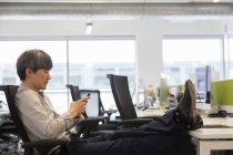 Empresário usando telefone inteligente com os pés na mesa de escritório — Fotografia de Stock