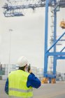 Dock worker with walkie-talkie watching crane at shipyard — Stock Photo