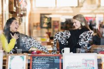 Счастливые юные подруги с одинаковыми свитерами в витрине кафе — стоковое фото