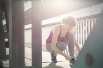 Junge Läuferin bindet Schuh auf sonnigem Bürgersteig — Stockfoto