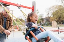 Giocoso nonno spingendo nipote su altalena parco giochi — Foto stock
