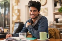 Portrait confident young male college student studying at cafe table — Stock Photo