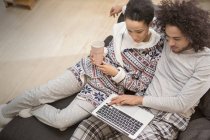 Casal afetuoso em pijama relaxante, usando laptop no sofá — Fotografia de Stock