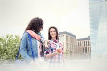 Young women friends with coffee walking in city — Stock Photo