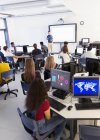 Étudiants du secondaire aux ordinateurs à l'écoute de l'enseignant à l'écran de projection en classe — Photo de stock