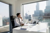 Empresário atencioso com papelada em escritório ensolarado, moderno e urbano — Fotografia de Stock