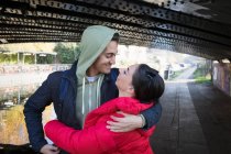 Feliz, afetuoso jovem casal abraçando sob ponte urbana — Fotografia de Stock