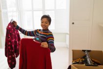 Sorrindo mulher desempacotando roupas de caixa móvel no quarto — Fotografia de Stock