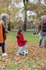 Бабушка и дедушка играют в футбол с внучкой в осеннем парке — стоковое фото