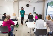 Estudiantes universitarios comunitarios viendo a instructor liderando lección en el aula - foto de stock