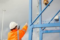 Dock worker with walkie-talkie directing crane at shipyard — Stock Photo