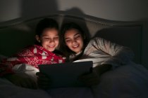 Chicas viendo la película en la tableta digital en dormitorio oscuro - foto de stock