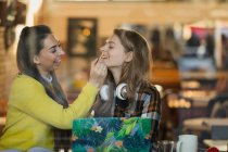 Young woman applying lip gloss to friends lips in cafe window — Stock Photo