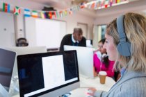 Estudante universitária da comunidade feminina com fones de ouvido usando computador em sala de aula de laboratório de informática — Fotografia de Stock