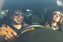 Feliz jovem casal vestindo óculos de sol no carro — Fotografia de Stock