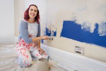 Portrait happy woman in overalls painting wall — Stock Photo