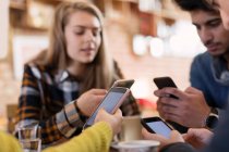 Amigos adultos jóvenes usando teléfonos inteligentes en la cafetería - foto de stock