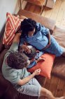 Pregnant young family using smart phone on living room sofa — Stock Photo