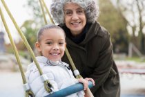 Ritratto sorridente nonna e nipote che giocano sull'altalena al parco giochi — Foto stock