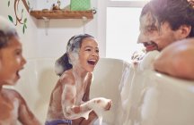Filhas brincalhões na banheira limpando bolhas no rosto dos pais — Fotografia de Stock