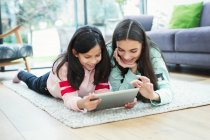 Hermanas sonrientes usando tableta digital en el piso de la sala de estar - foto de stock