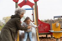 Grandmother playing with granddaughter on playground slide — Stock Photo