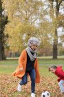 Playful grandmother playing soccer with granddaughter in autumn park — Stock Photo