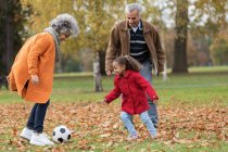 Grand-parents jouant au football avec petite-fille dans le parc d'automne — Photo de stock