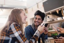 Amigos adultos jóvenes felices usando teléfonos inteligentes en la cafetería - foto de stock