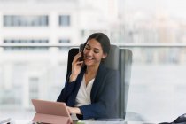 Усміхнена бізнес-леді розмовляє на смартфоні в офісі — стокове фото